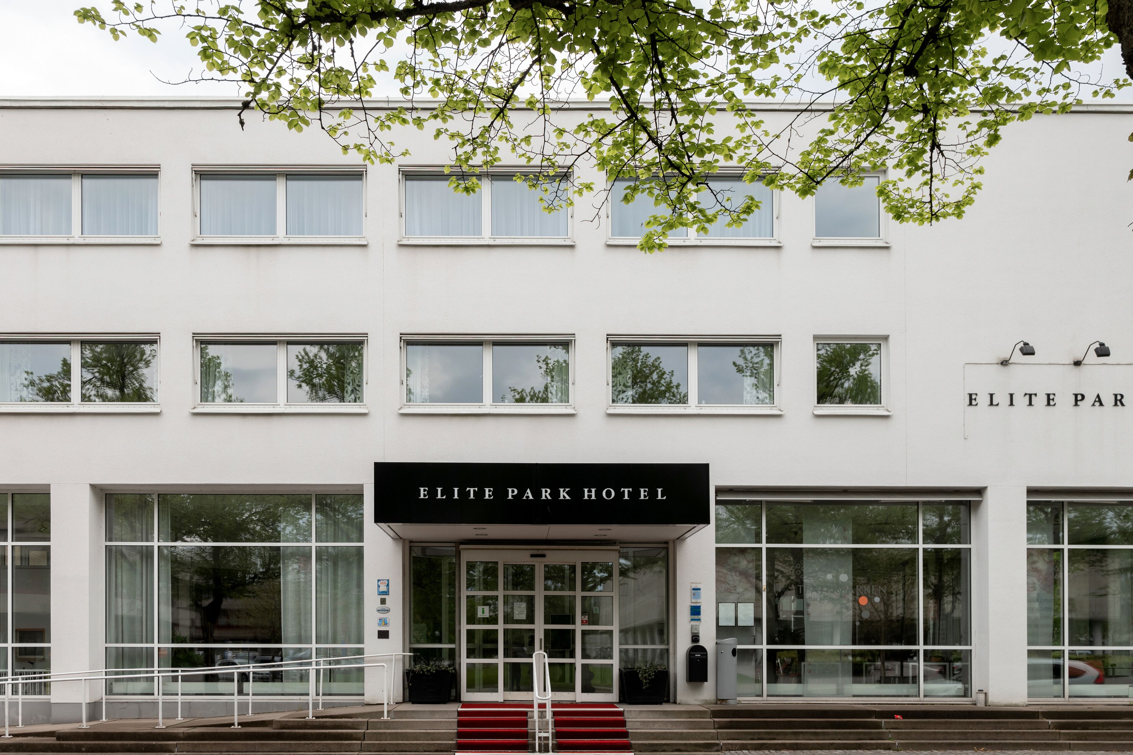 The exterior of the Elite Park Hotel with a modern facade, large windows, and a prominent entrance with steps leading up to the door.