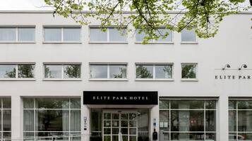 The exterior of the Elite Park Hotel with a modern facade, large windows, and a prominent entrance with steps leading up to the door.