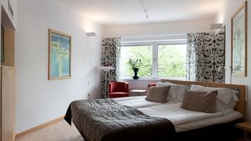 Une chambre d’hôtel moderne avec un grand lit, une petite table, une chaise rouge et une fenêtre avec des rideaux.