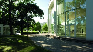 A modern building with large glass windows, a paved pathway, and surrounding greenery. - Elite Park Hotel Växjö (Växjö)