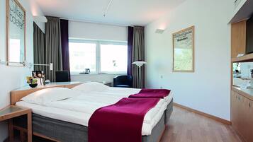 Een hotelkamer met een groot bed, een bureau met stoel, een raam met gordijnen, een bureaulamp en een aan de muur bevestigde televisie.