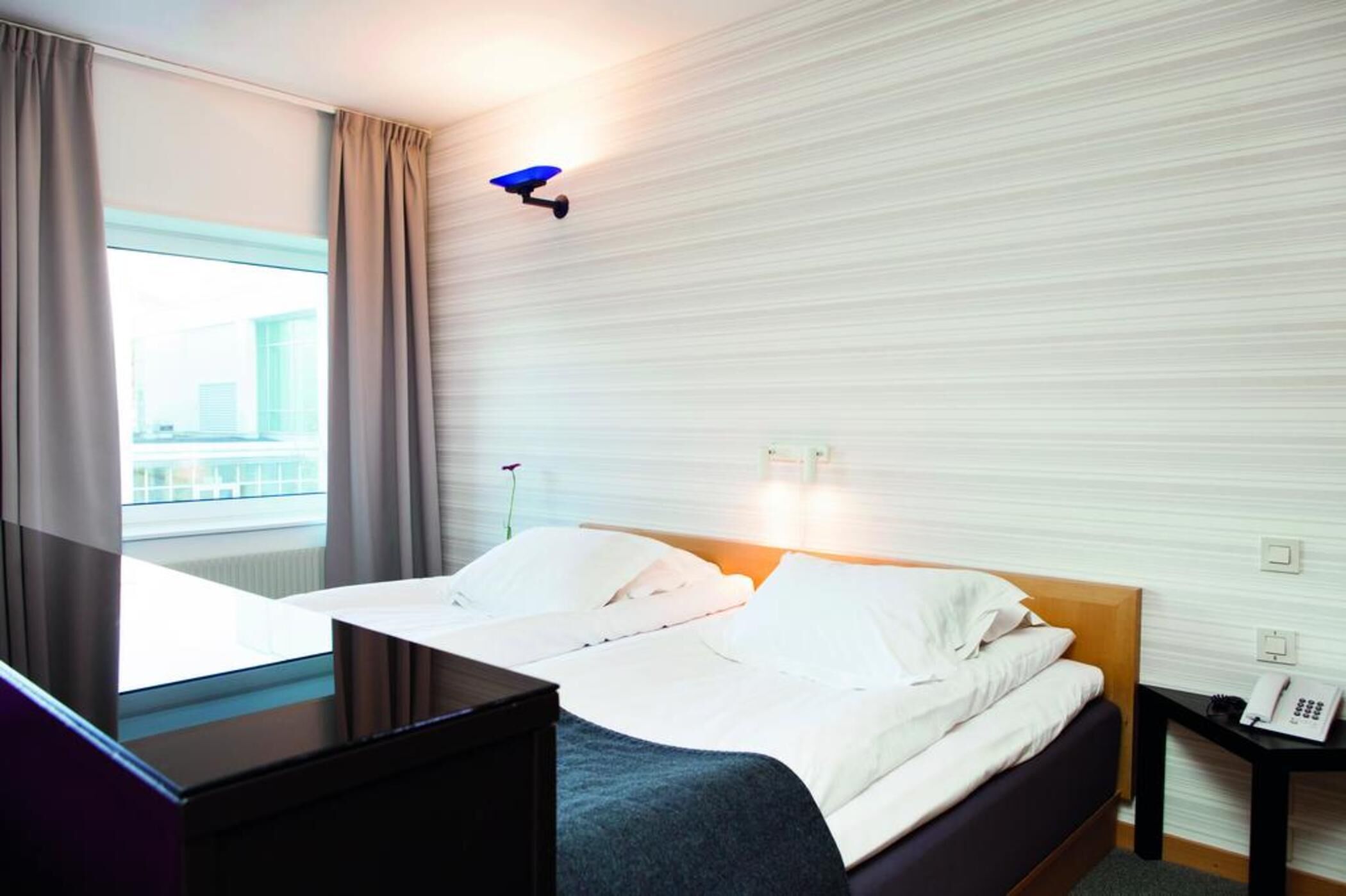Habitación de hotel con cama, escritorio, teléfono y ventana con cortinas.