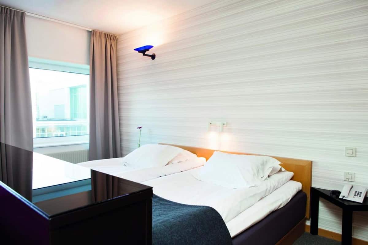 A hotel room with a bed, a desk, a telephone, and a window with curtains.