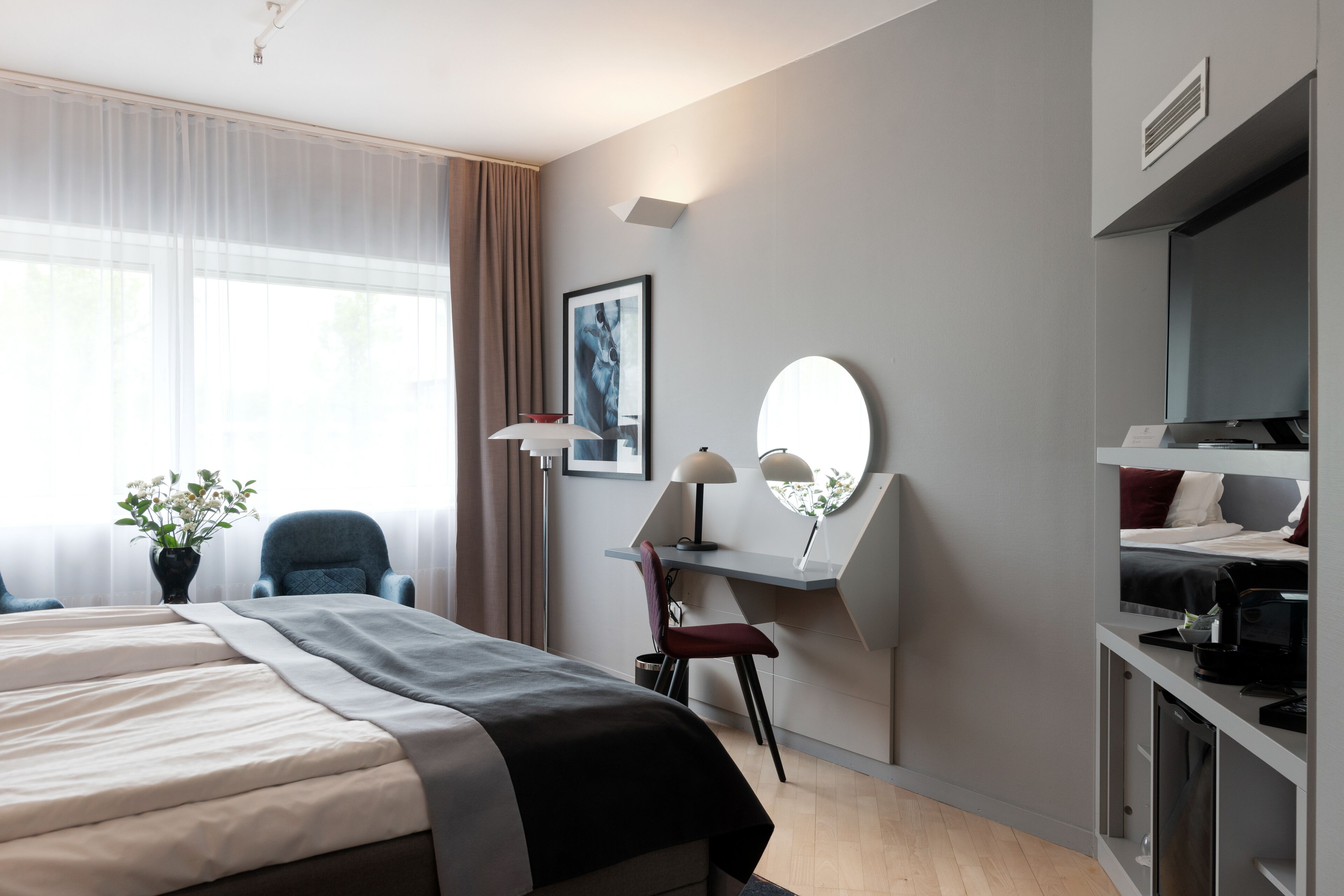 A hotel room with a bed, desk, chair, and a large mirror.
