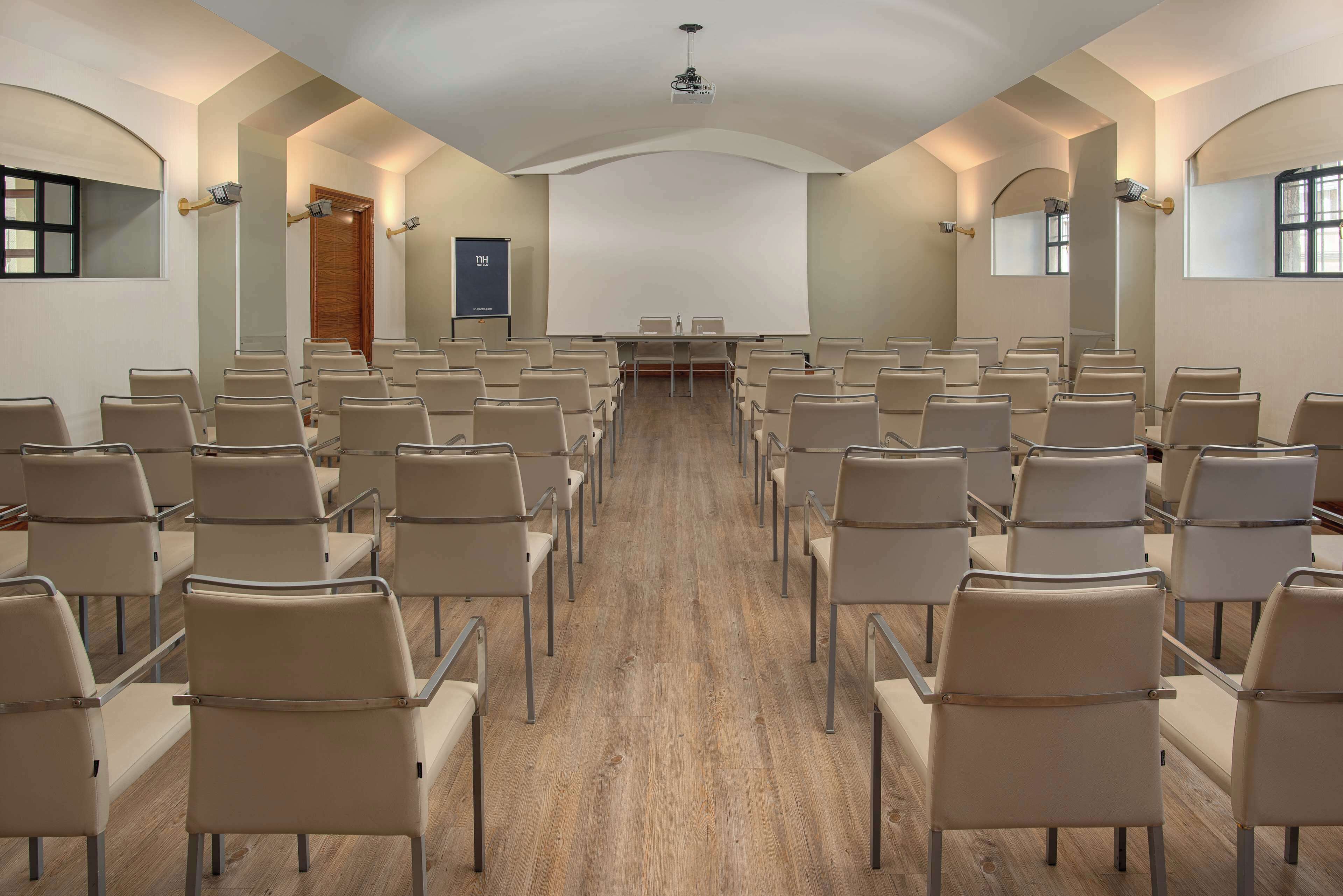 A conference room with rows of chairs facing a large screen, wooden flooring, and arched ceiling design.
