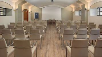Un salón de conferencias con filas de sillas orientadas hacia una pantalla grande, suelo de madera y diseño de techo abovedado.