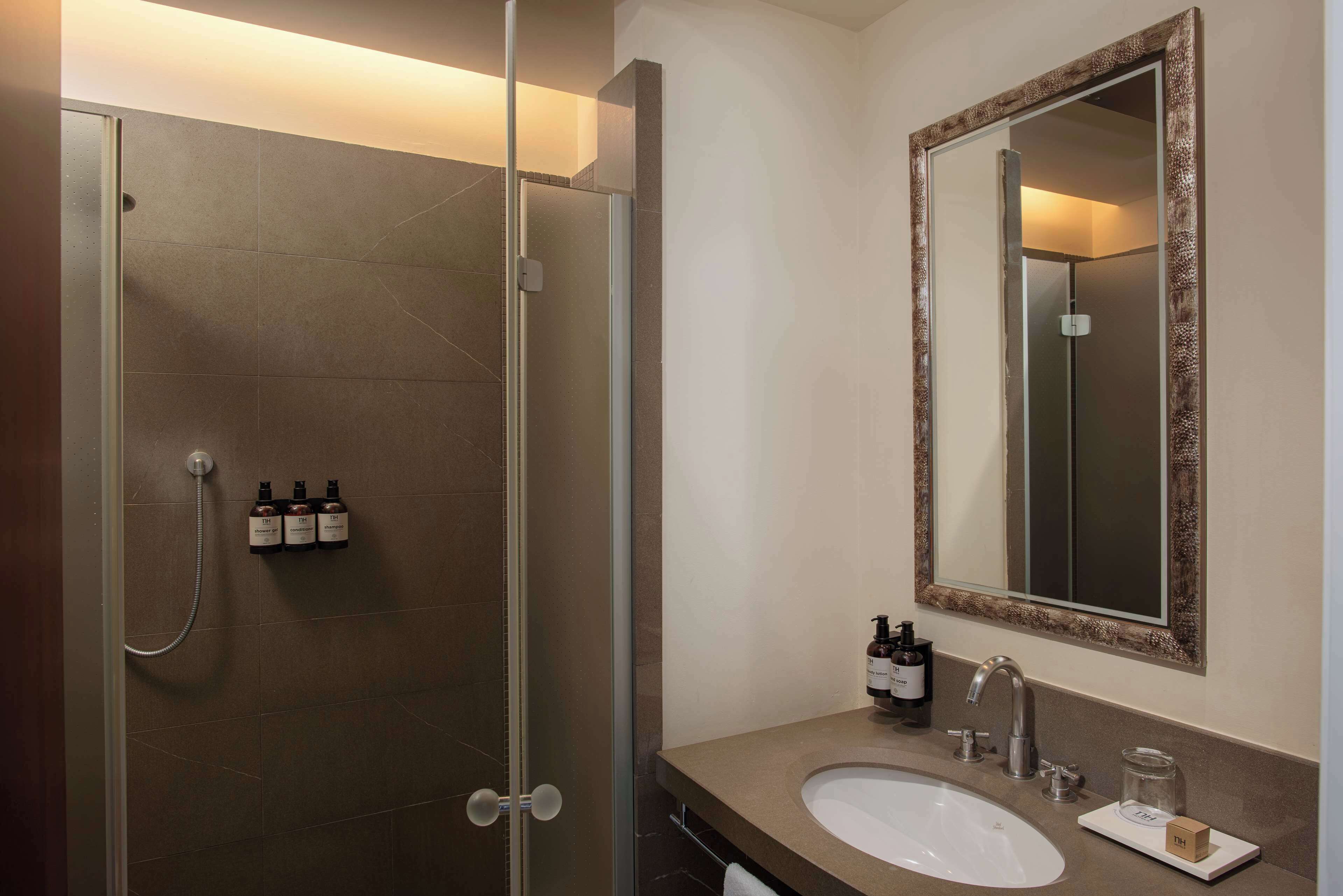 A modern bathroom with a glass-enclosed shower, a sink with a mirror, and toiletries on the wall.
