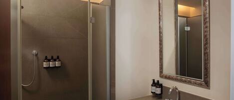 A modern bathroom with a glass-enclosed shower, a sink with a mirror, and toiletries on the wall.