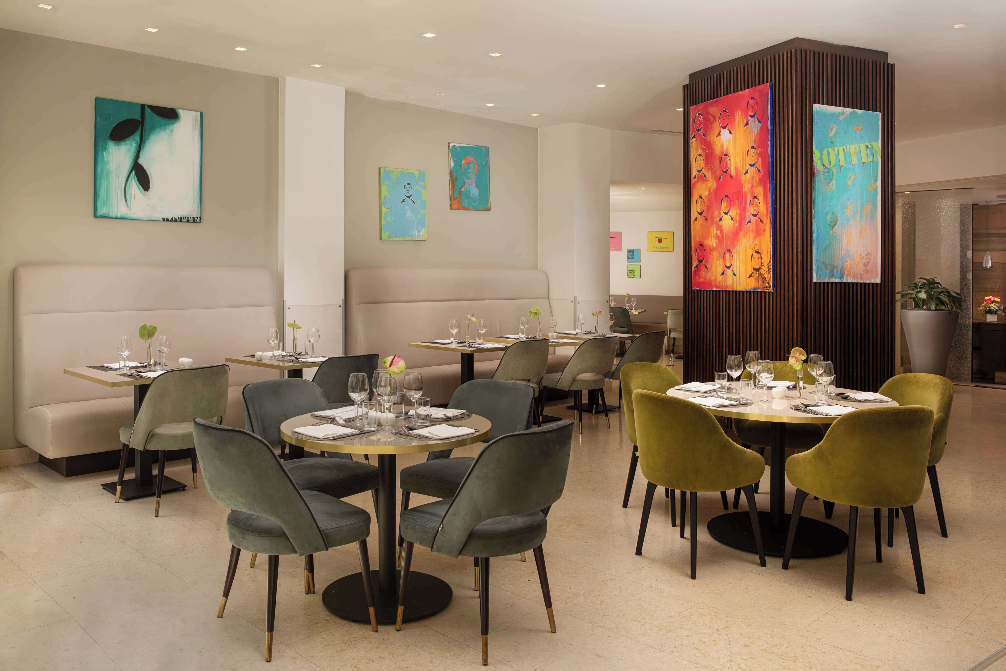 A modern dining area with round tables, grey and yellow chairs, and artwork on the walls.