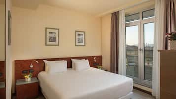 A hotel room with a large bed, two bedside tables, a nightstand, a window with curtains, and a view of buildings outside.