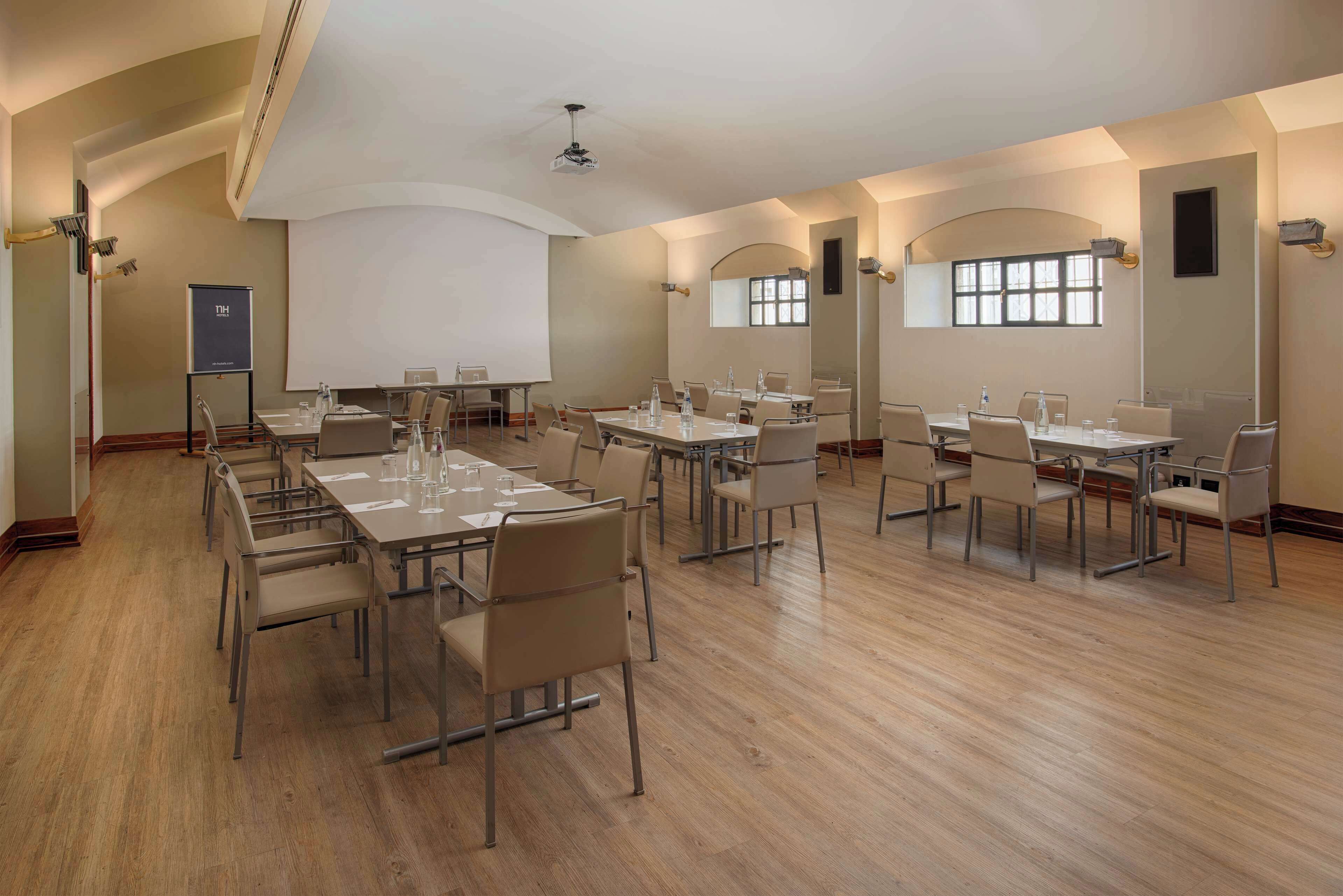 Una sala conferenze con più tavoli e sedie, uno schermo per proiettore e una grande finestra.