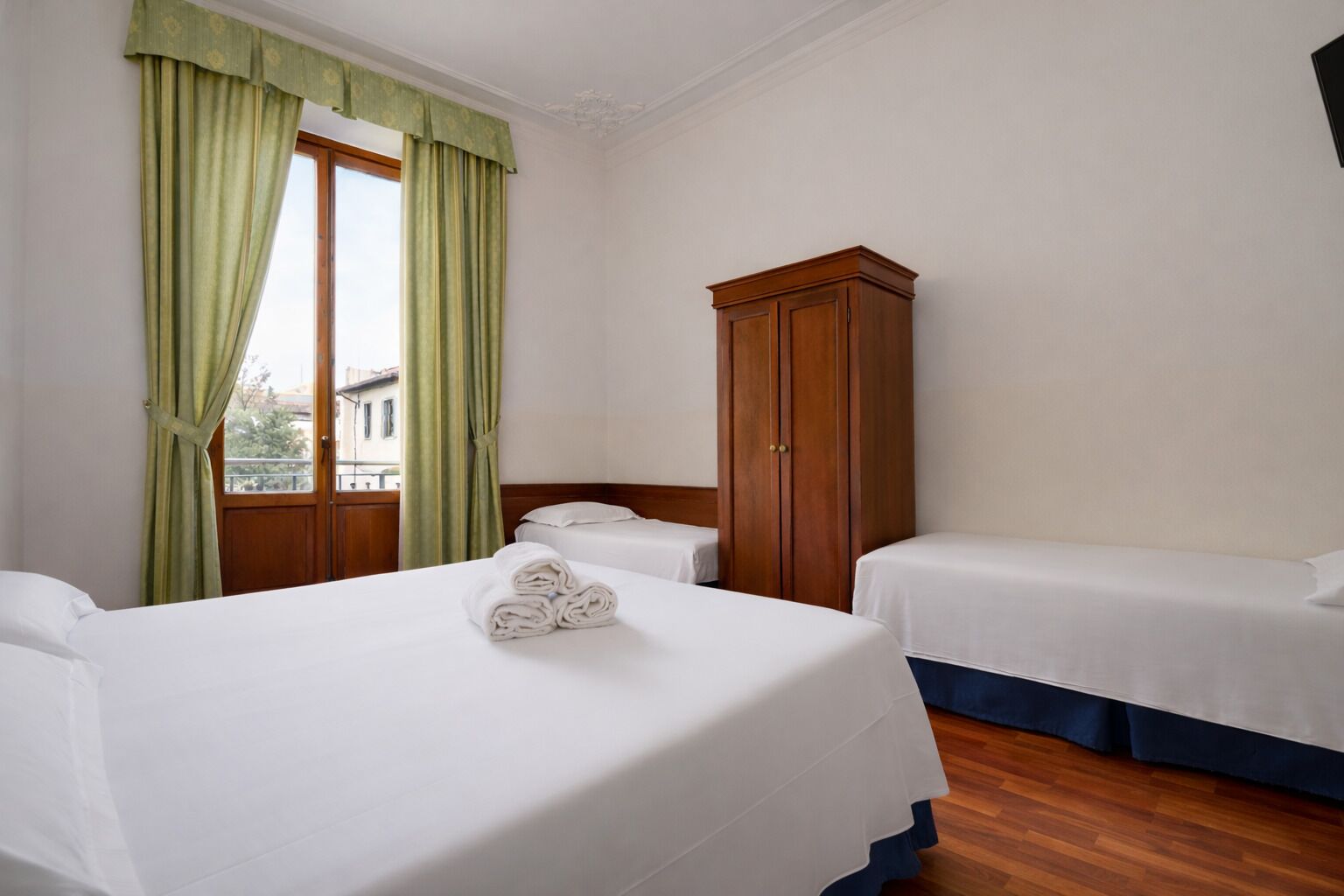 A hotel room with two beds, a wooden wardrobe, and a window with curtains.