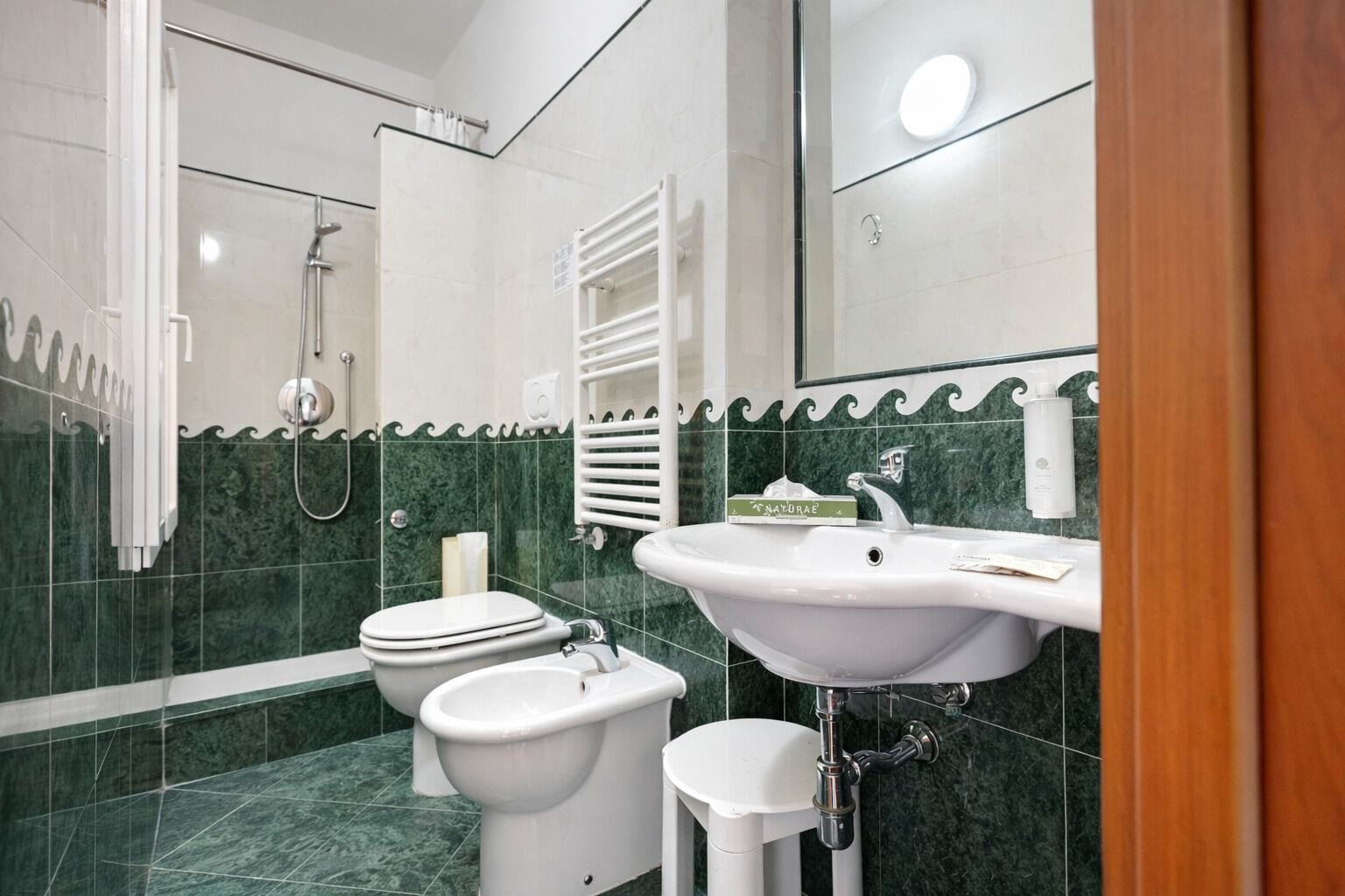 A bathroom with a shower, toilet, bidet, sink, and a towel rack.