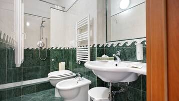 A bathroom with a shower, toilet, bidet, sink, and a towel rack.