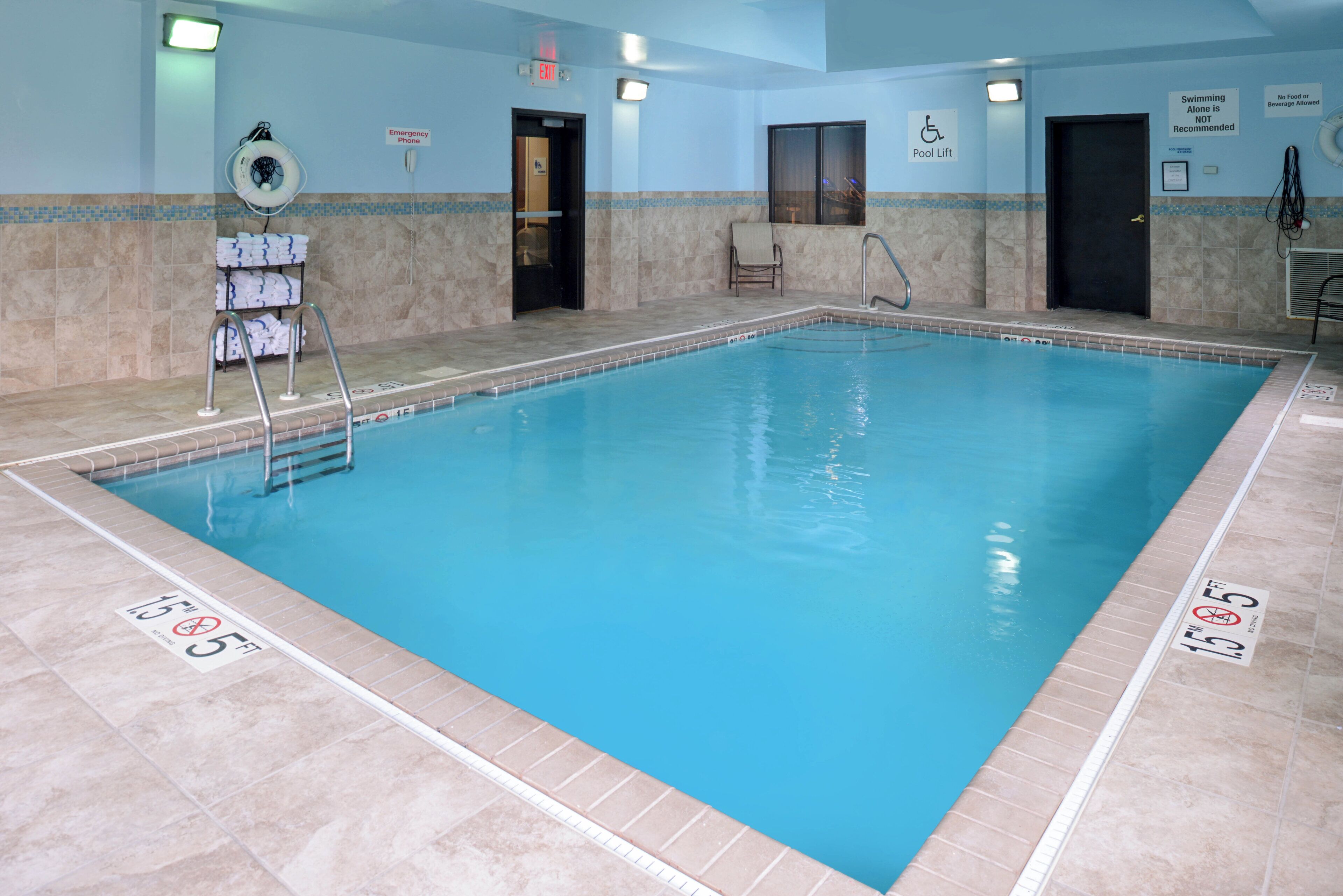 Una piscina interior con agua cristalina, líneas de profundidad marcadas y señalización de seguridad.