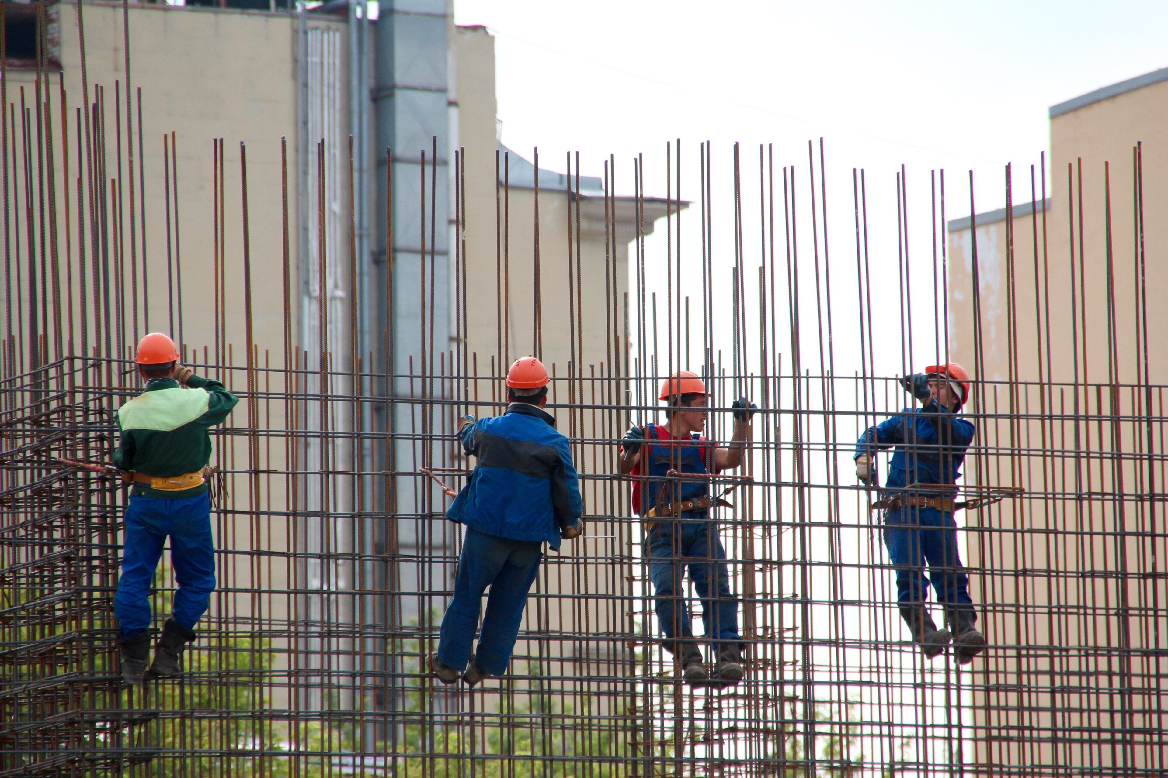 Treballadors a una obra de construcció amb escenari metàl·lic i barres verticals de metall.