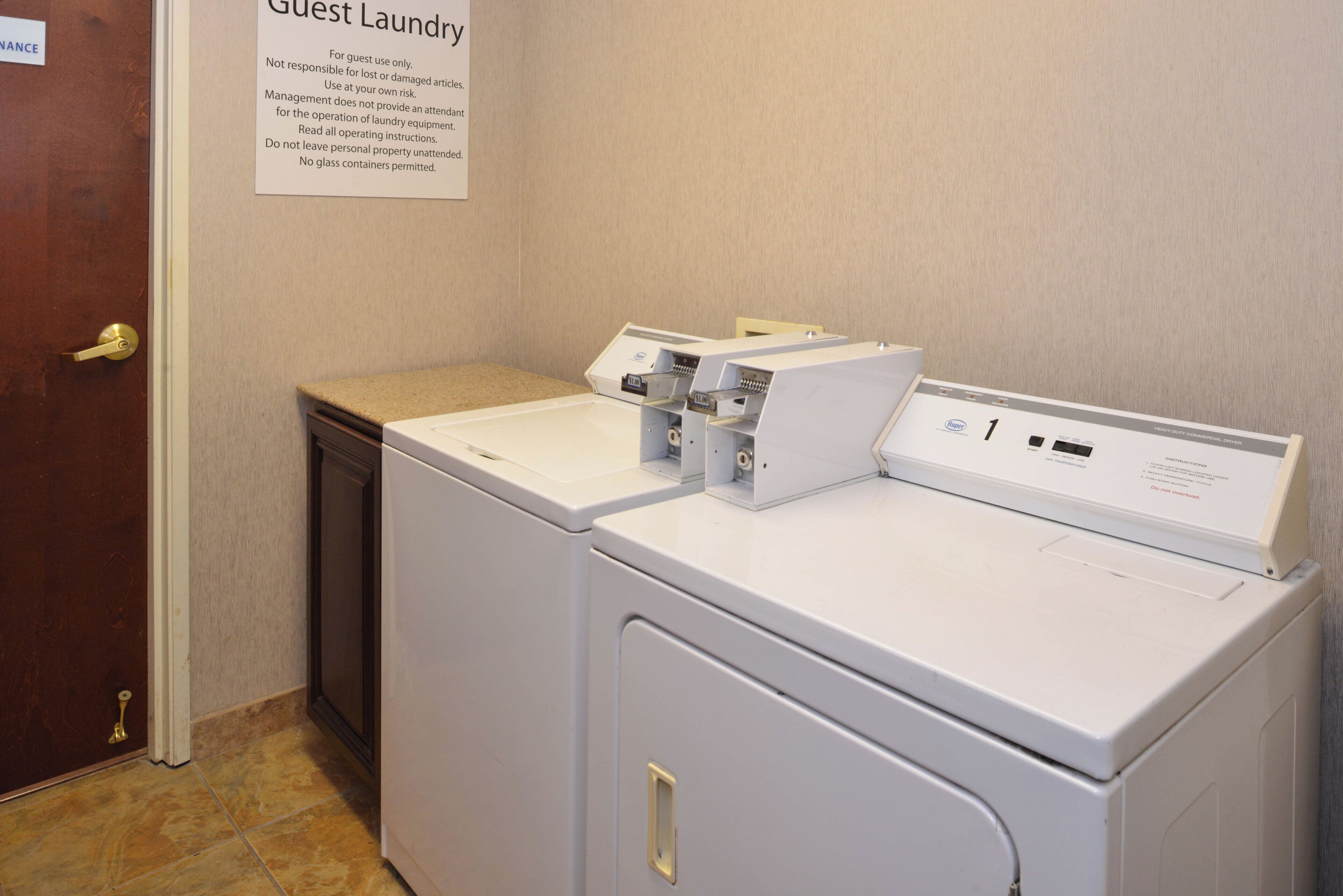 A guest laundry area with a front-loading washer and dryer, a sign with laundry instructions, and a door with a brass handle.