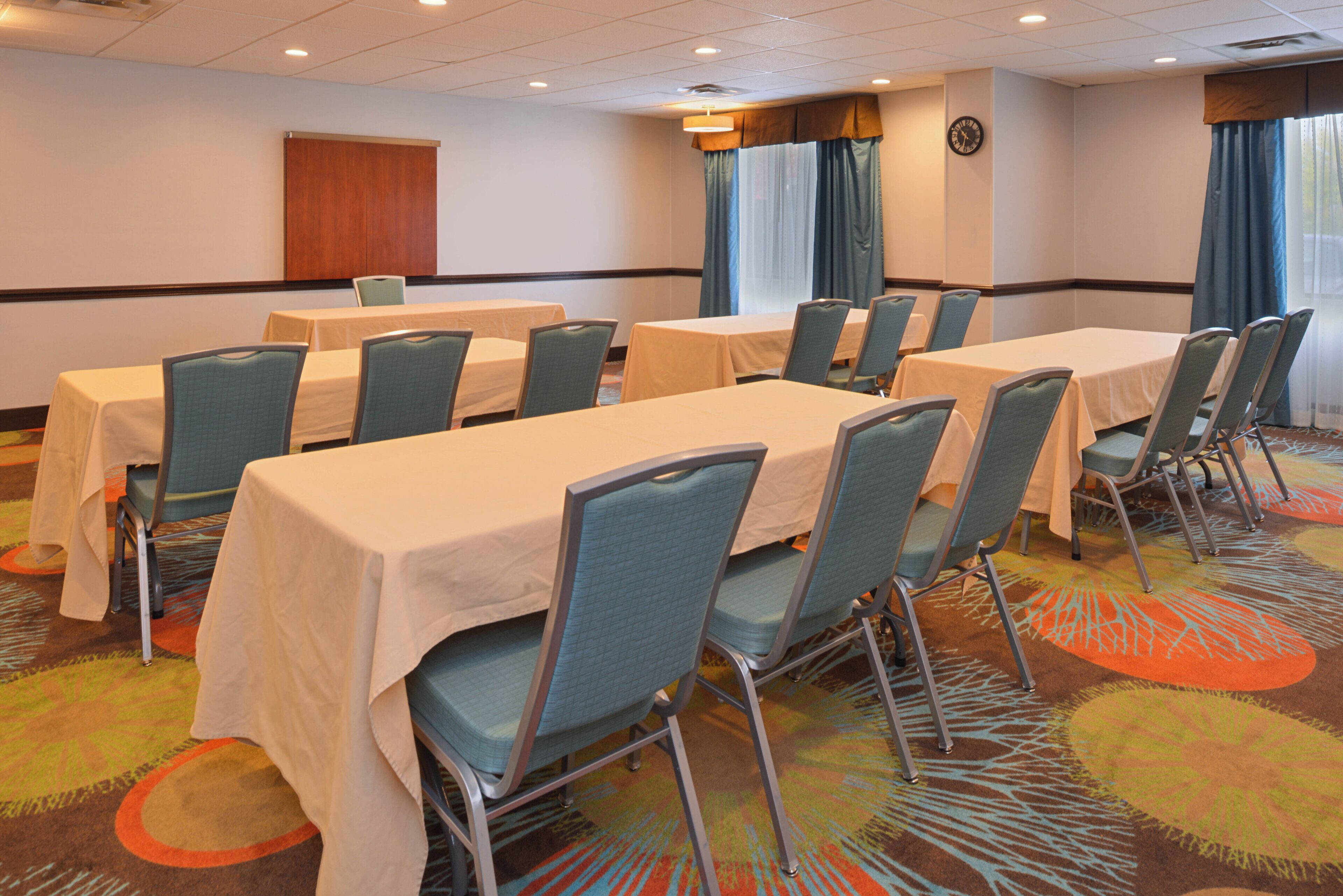 Une salle de conférence avec des tables et des chaises, une horloge au mur et une porte à l’arrière-plan.