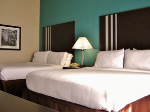 A hotel room with two beds, a nightstand with a lamp, and a framed picture on the wall.