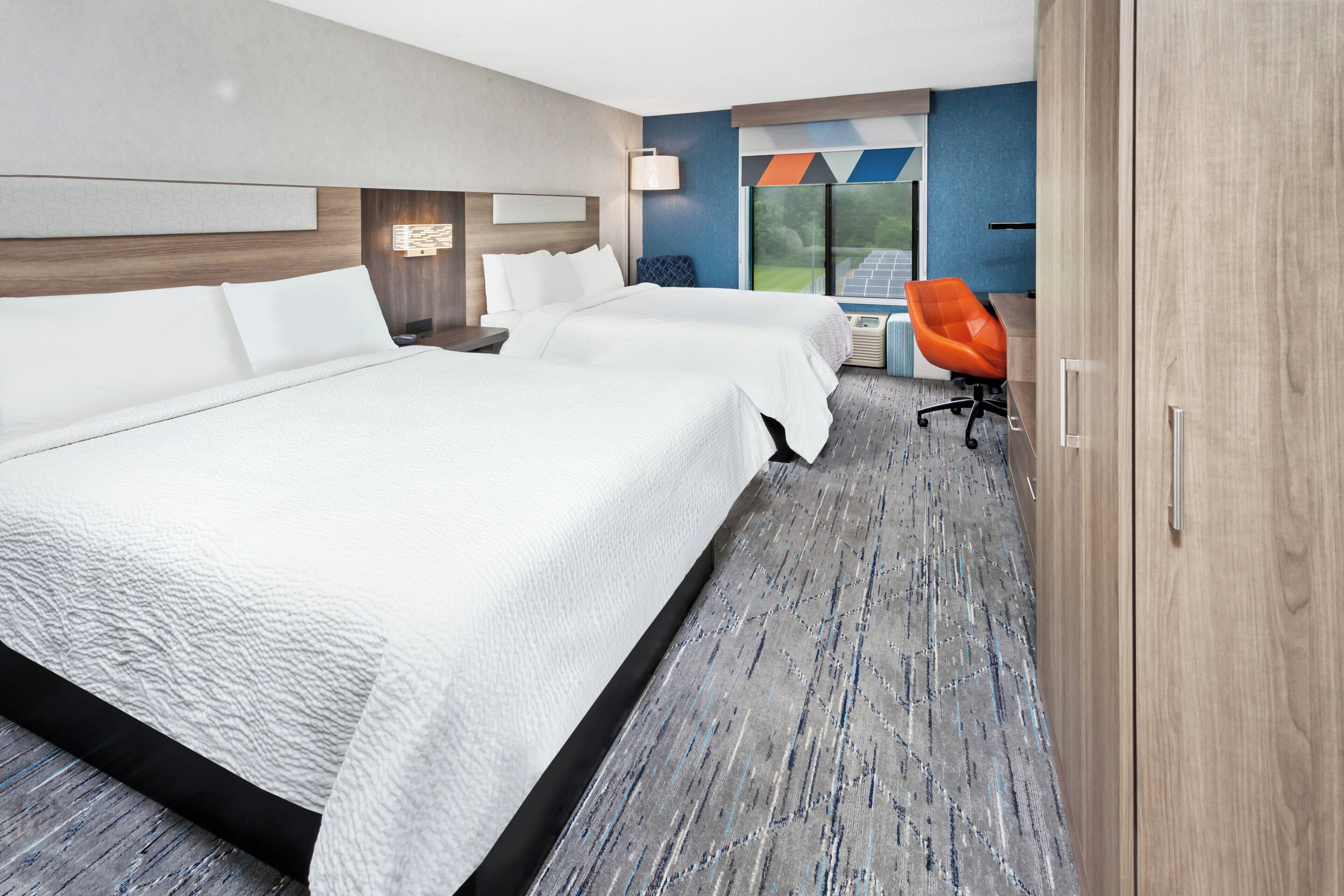 Quarto de hotel com duas camas, uma mesa e uma cadeira.