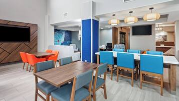 Un moderno vestíbulo de hotel con zona de comedor, un televisor en la pared y una pared decorativa azul.