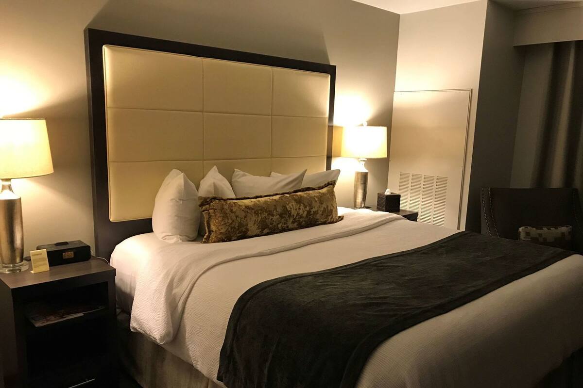 A hotel room with a large bed, two bedside tables, a headboard, and two lamps.