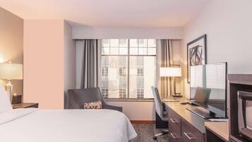 Une chambre d’hôtel comprenant un lit, un bureau avec un ordinateur, une chaise et un téléviseur.