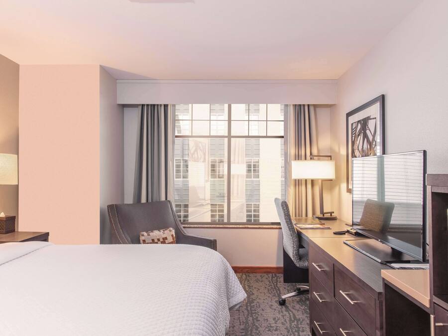 Una habitación de hotel con una cama, un escritorio con computadora, una silla y un televisor.