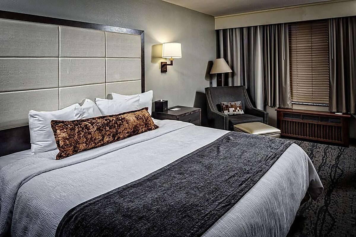 A hotel room with a large bed, a nightstand, a chair, a lamp, and a window with curtains.