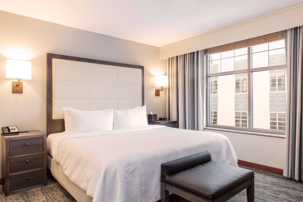 A hotel room with a large bed, bedside tables, a desk, and a window with curtains.