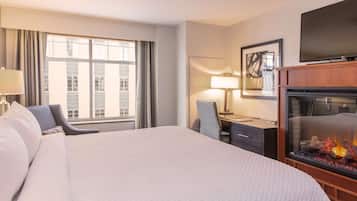 Ein Hotelzimmer mit einem großen Bett, einem Schreibtisch mit Stuhl, einem Fernseher und einem Kamin.