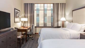 A hotel room with two beds, a desk, a chair, a TV, and a window with curtains.