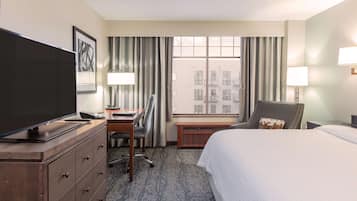 Une chambre d’hôtel comprenant un lit, un bureau avec une chaise, une télévision, une fenêtre avec des rideaux et une lampe.