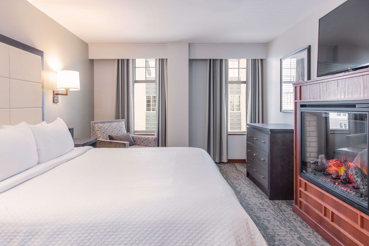 Una habitación de hotel con una cama grande, una silla, un aparador y una chimenea.