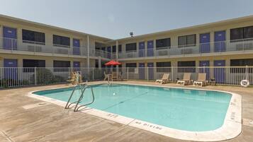 A pool area with a no diving sign, lounge chairs, and a red umbrella.
