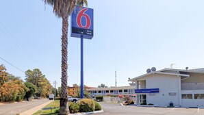 Un motel con un llamativo letrero con el número '6', un estacionamiento y un edificio con un cartel de 'WELCOME'.