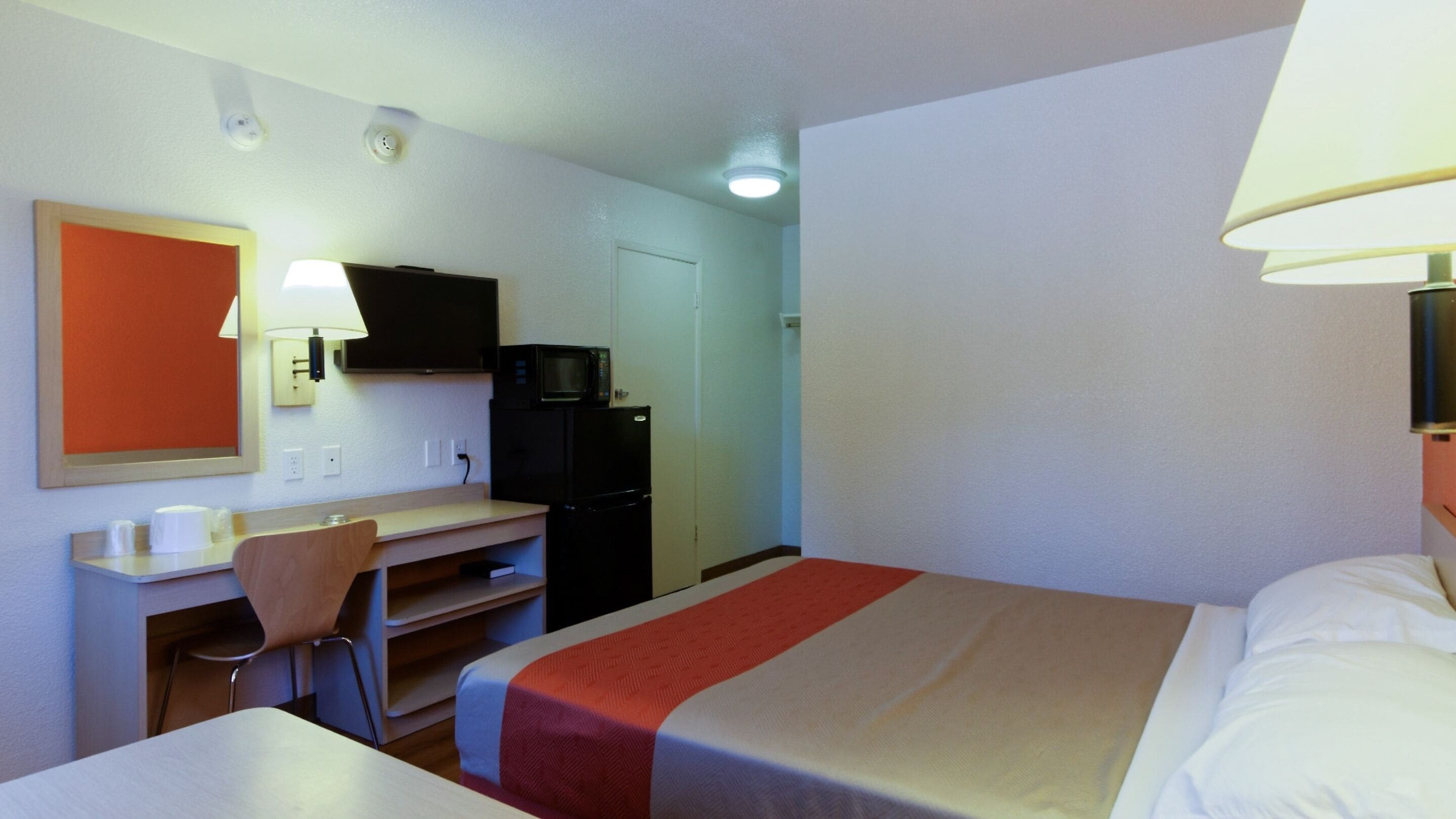 A hotel room with a bed, a desk with a chair, a television, and a microwave.