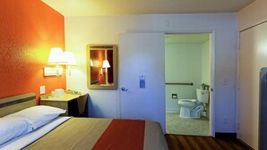 A hotel room with a bed, bedside table, lamp, and a door leading to a bathroom. - Motel 6 Chico, CA (Chico)