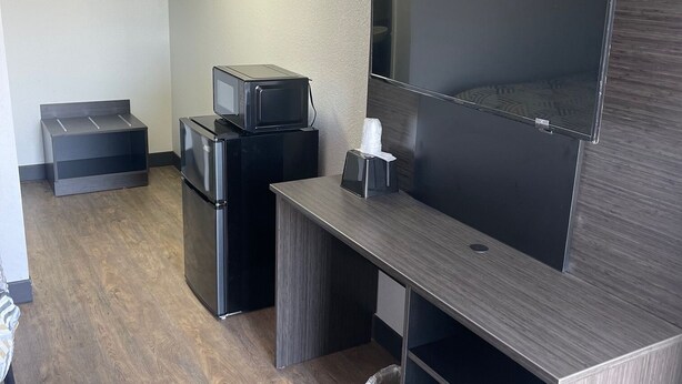 A compact hotel room with a kitchenette, a flat-screen TV mounted on the wall, a small refrigerator, and a microwave. - Motel 6 Wichita, KS (Wichita)