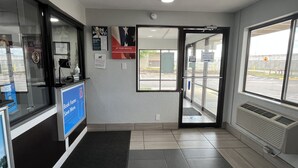 A reception area with a check-in counter, a door leading outside, and a window with a view of the street. - Motel 6 Wichita, KS (Wichita)