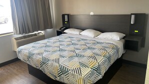 A hotel room with a large bed, a bedside table with a phone, a wall-mounted light, and a window with curtains. - Motel 6 Wichita, KS (Wichita)
