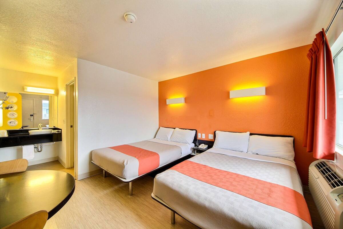 A hotel room with two beds, a bathroom with a sink, and a table.
