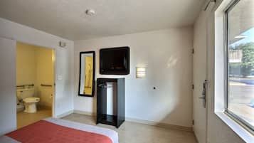 Habitación de hotel con cama, televisión, espejo, una mesita y ventana con vistas al exterior.