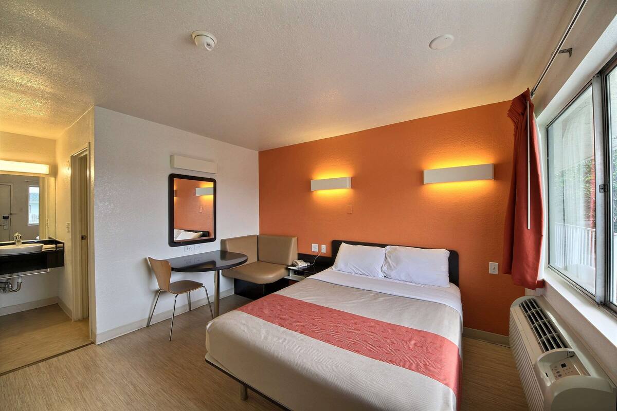 A hotel room with a bed, a desk, a chair, a bathroom, and a window.