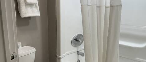 Un baño con inodoro, bañera con cortina de ducha y toalla colgada en la pared.