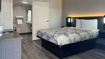 A hotel room with a bed, bedside table, and a desk with a chair.