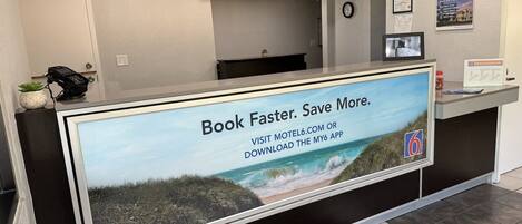 A reception desk with a large screen displaying a beach scene and text promoting a booking app.
