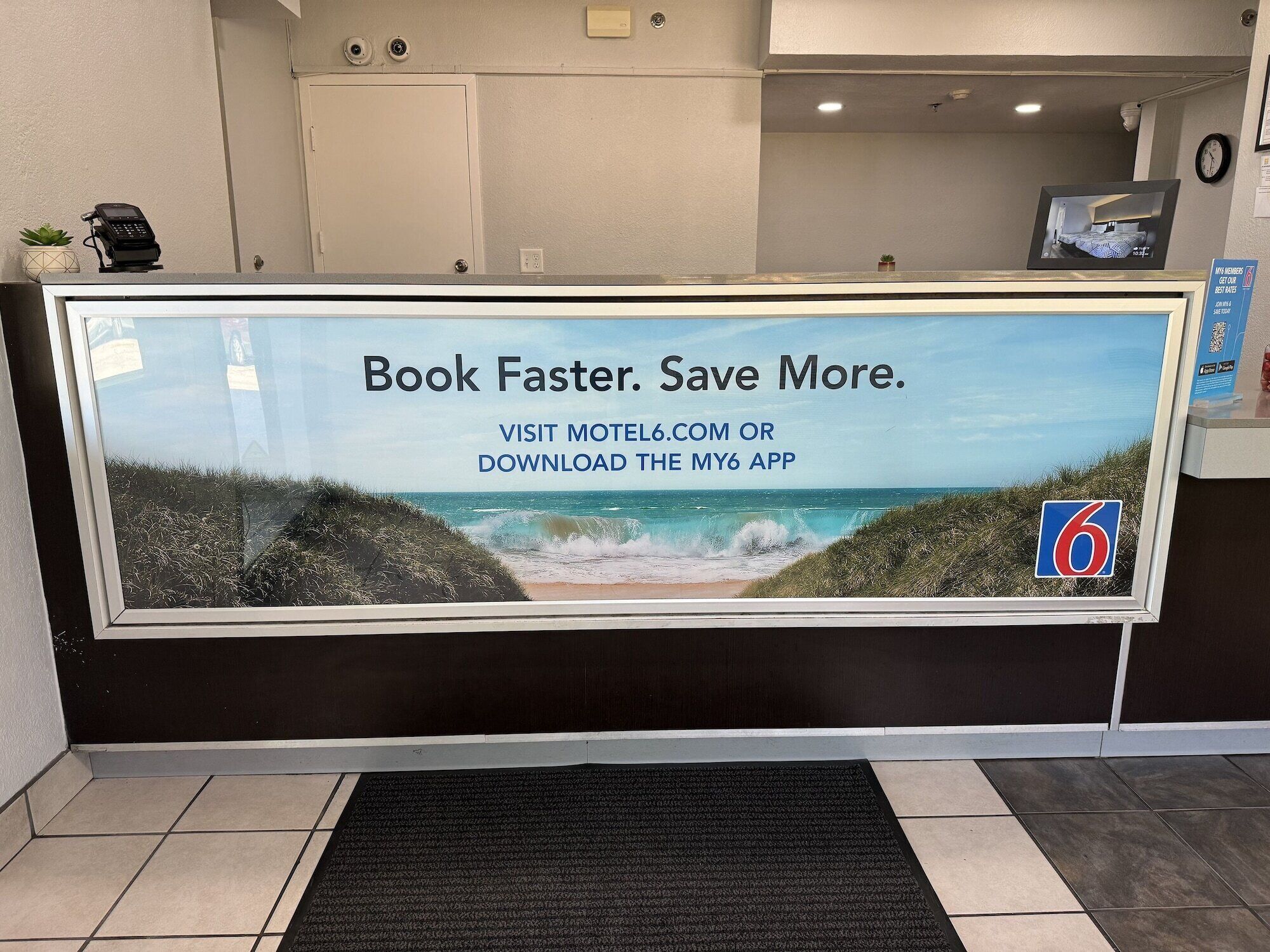 A reception desk with a large advertisement for booking faster and saving more at Motel6.com or downloading the My6 app.
