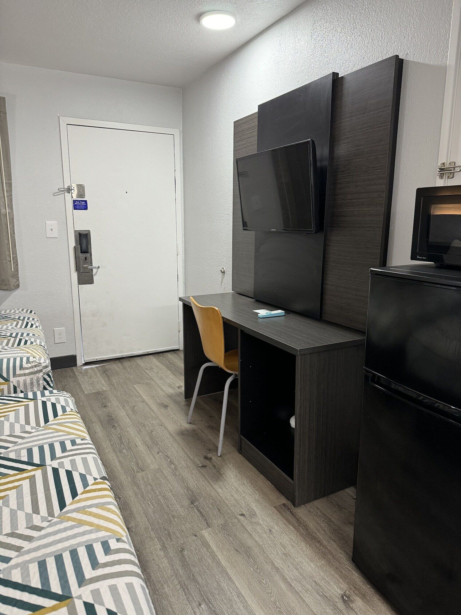 A hotel room with a bed, a desk, a chair, a television, and a refrigerator.
