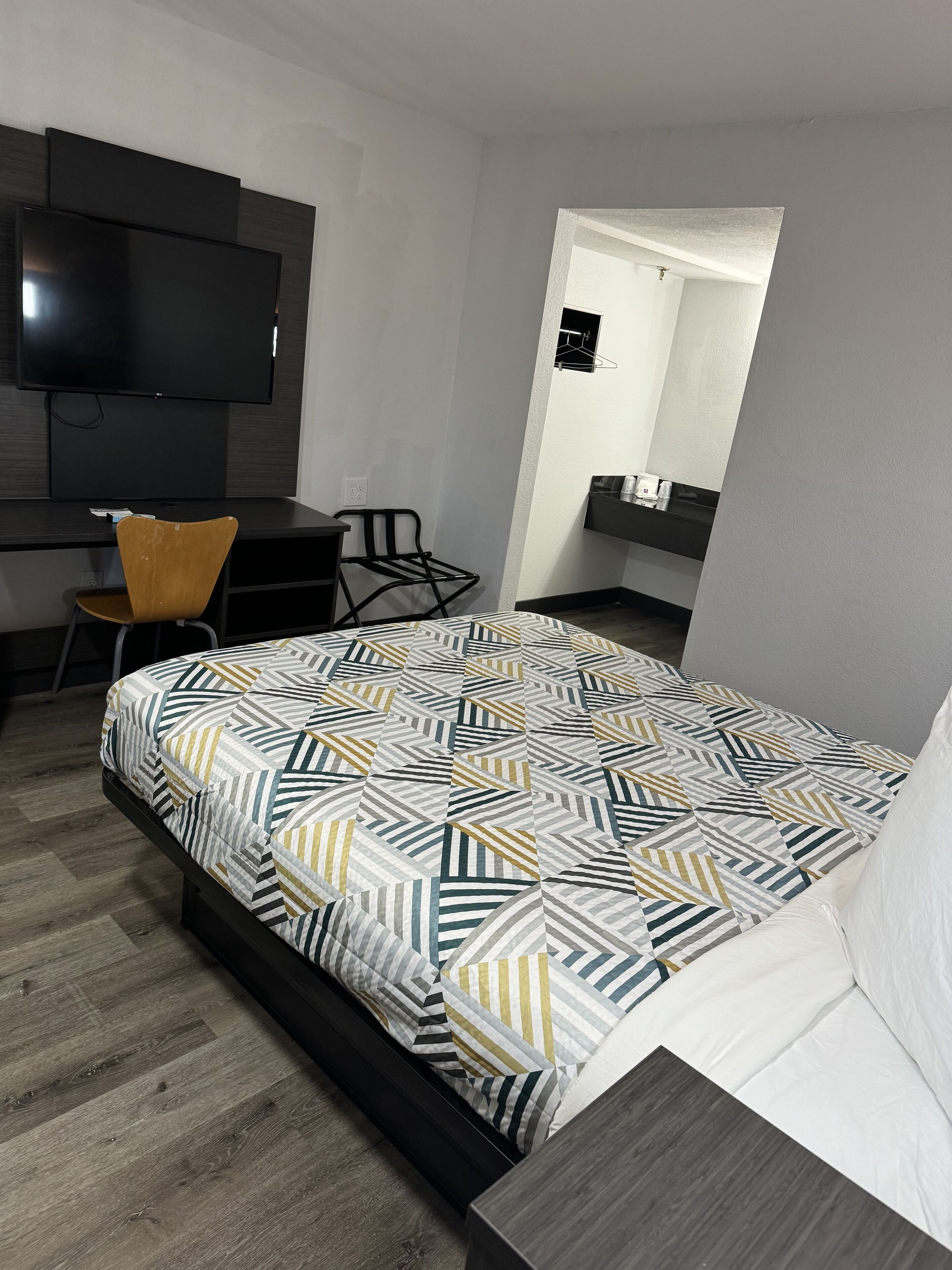 Une chambre d’hôtel moderne dotée d’un grand lit, d ’un téléviseur à écran plat fixé au mur, d’un bureau avec une chaise et d’une petite salle de bain visible à travers une porte ouverte.
